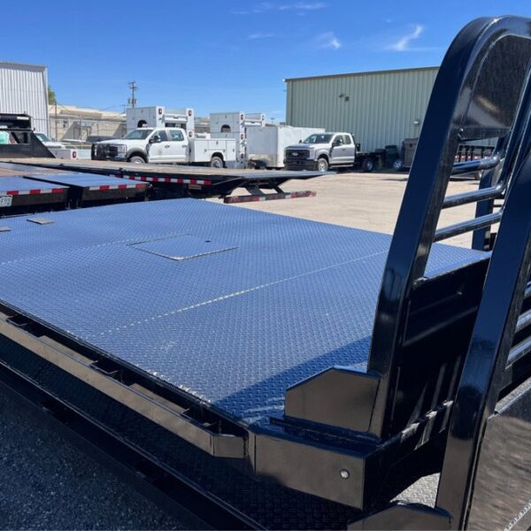 Two Black steel flatbed truck beds with diamond plate deck and headache rack stacked in a full trailer lot