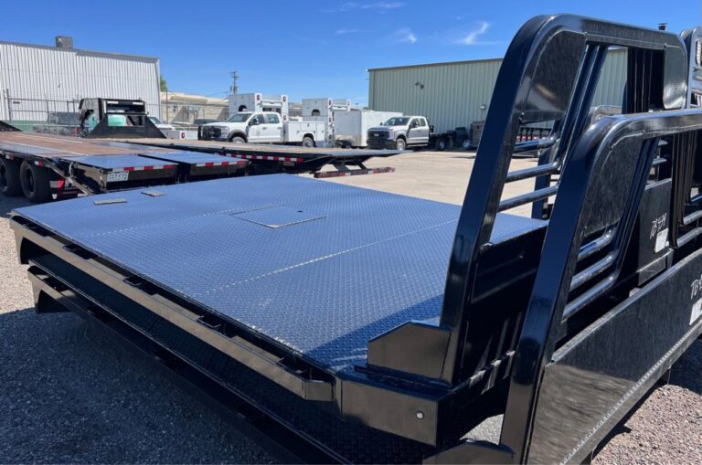 Two Black steel flatbed truck beds with diamond plate deck and headache rack stacked in a full trailer lot