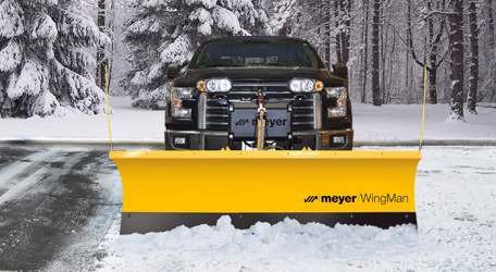 Black truck with yellow Meyer WingMan snow plow clearing snow on road surrounded by snow-covered trees in winter landscape.