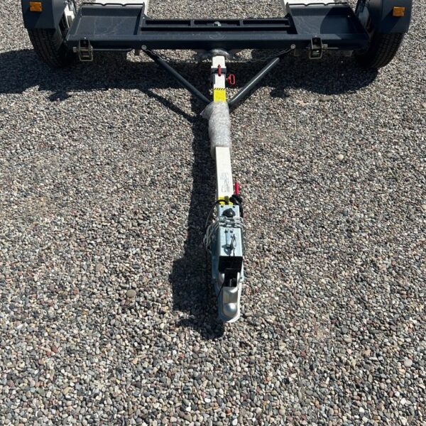 Car tow dolly with two ramps, black frame, and white hitch arm parked on gravel surface