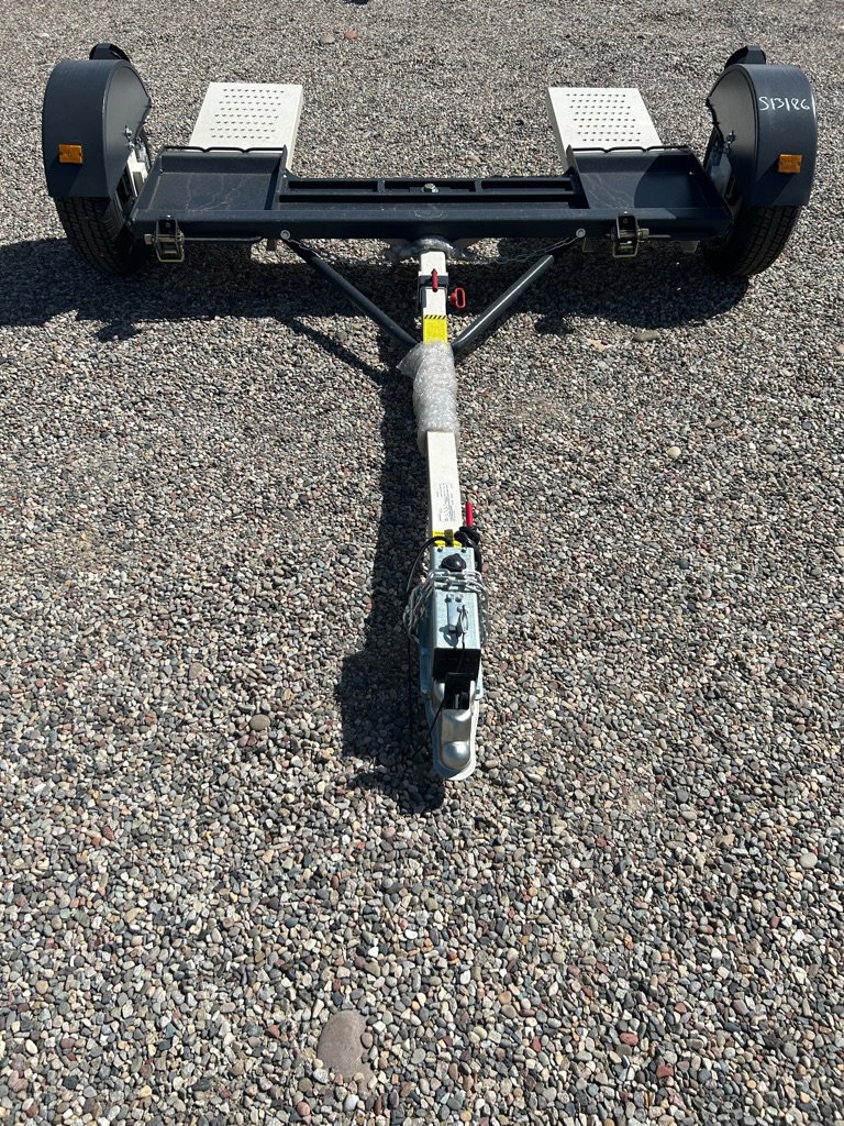 Car tow dolly with two ramps, black frame, and white hitch arm parked on gravel surface