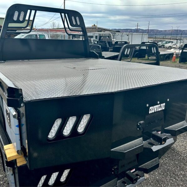 Black Crownline flatbed truck bed with diamond plate deck and headache rack, parked on gravel