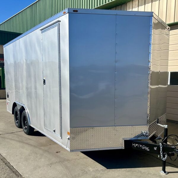 Silver enclosed cargo trailer with side door, dual axles, and diamond plate trim parked on pavement