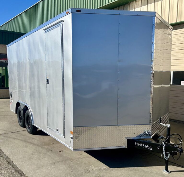 Silver enclosed cargo trailer with side door, dual axles, and diamond plate trim parked on pavement