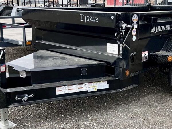 Black Iron Bull dump trailer with dual axles parked on gravel lot with other trailers visible in background.