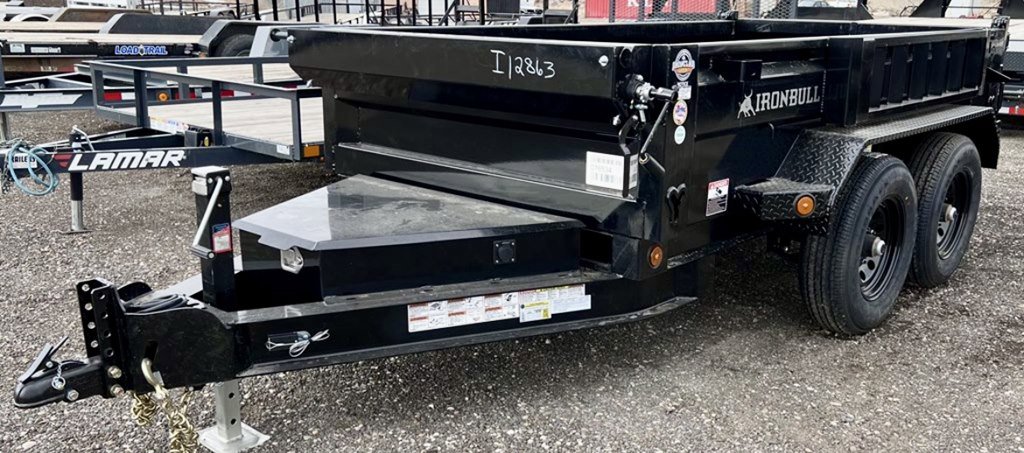 Black Iron Bull dump trailer with dual axles parked on gravel lot with other trailers visible in background.