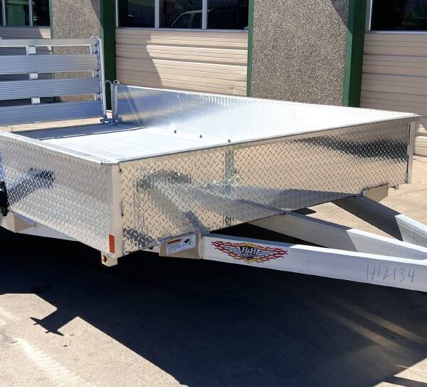 Silver aluminum utility trailer with diamond plate front, black wheel, and rear ramp gate, parked on concrete commercial driveway