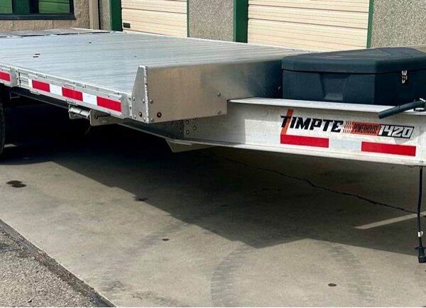 Silver Timpte 1420 aluminum car hauler trailer parked on pavement near a commercial building with garage doors.
