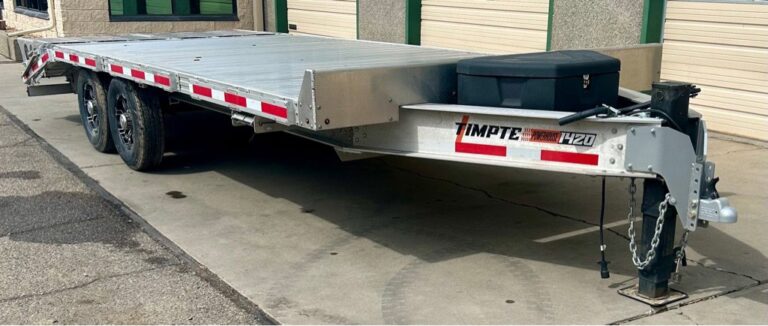 Silver Timpte 1420 aluminum car hauler trailer parked on pavement near a commercial building with garage doors.