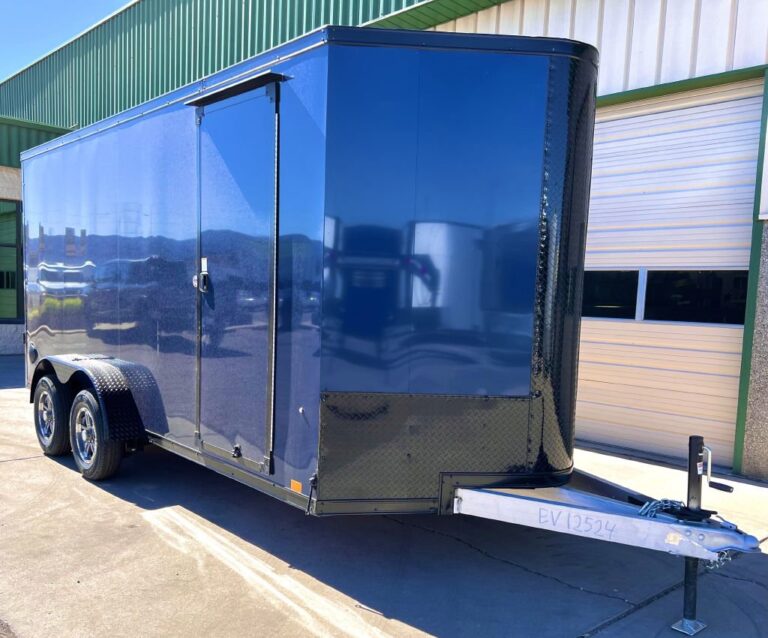 Dark blue enclosed cargo trailer with side door, dual axles, and diamond plate trim parked outside
