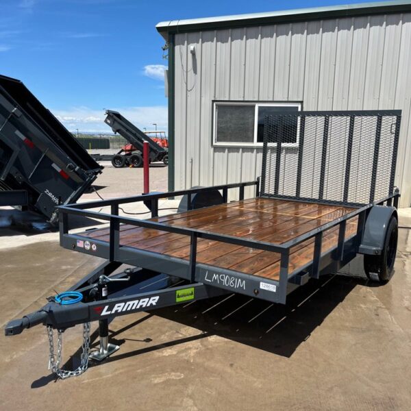 Freshly washed gray Lamar utility trailer with wood deck, mesh ramp gate, and single axle parked on wet concrete