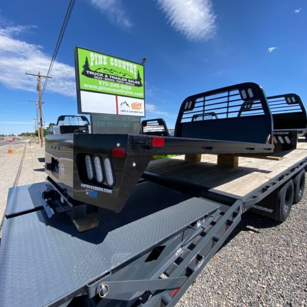 Black truck beds stacked on flatbed trailer in gravel lot near Pine Country Trailer Sales sign