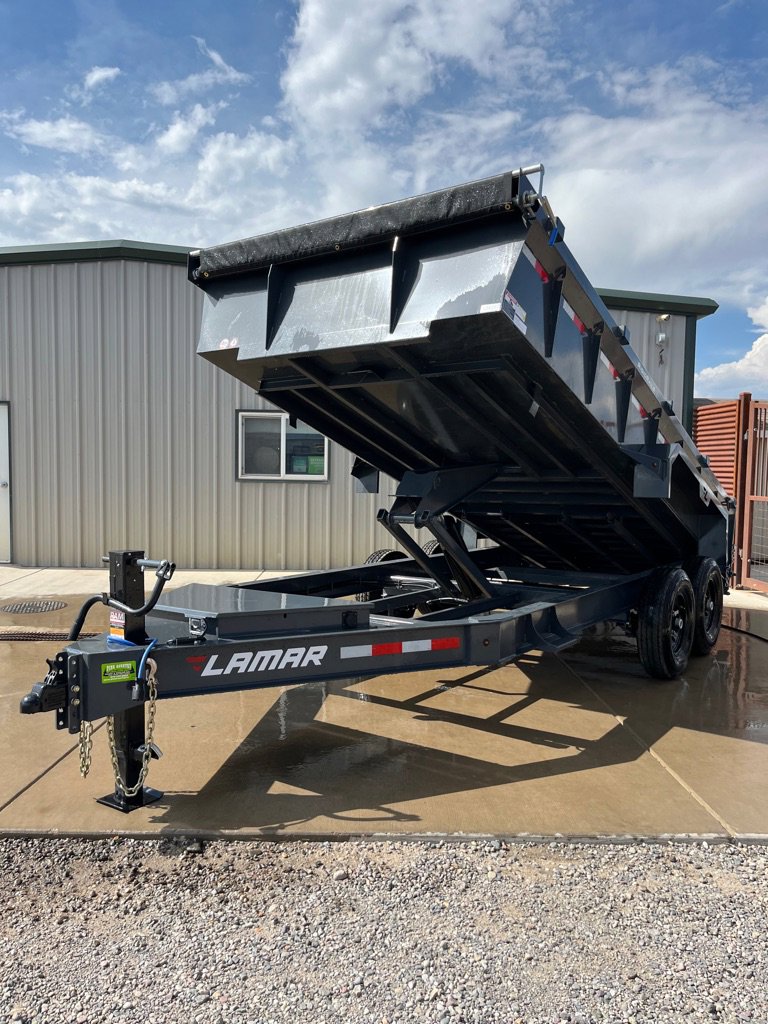 Dark blue Lamar dump trailer with raised bed, dual axles, tarp system, and red-white safety stripes