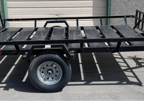 Black Echo utility trailer with metal grate floor and ramp gate, parked on concrete by beige garage doors.
