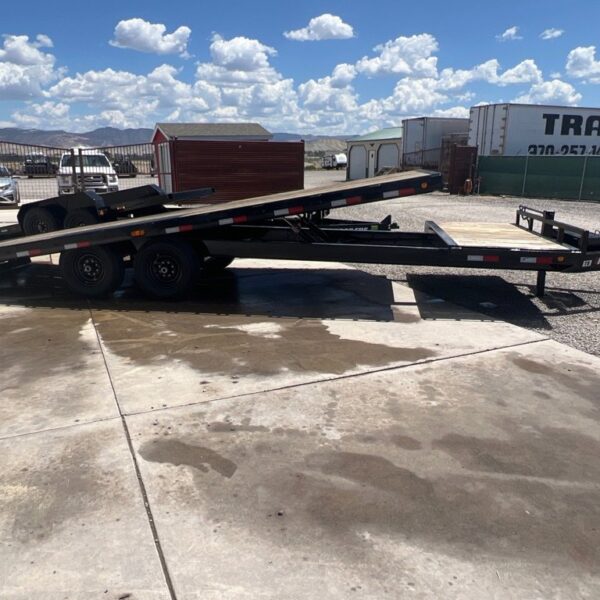 Black PJ tilt trailer with deck raised, parked on concrete trailer sales lot