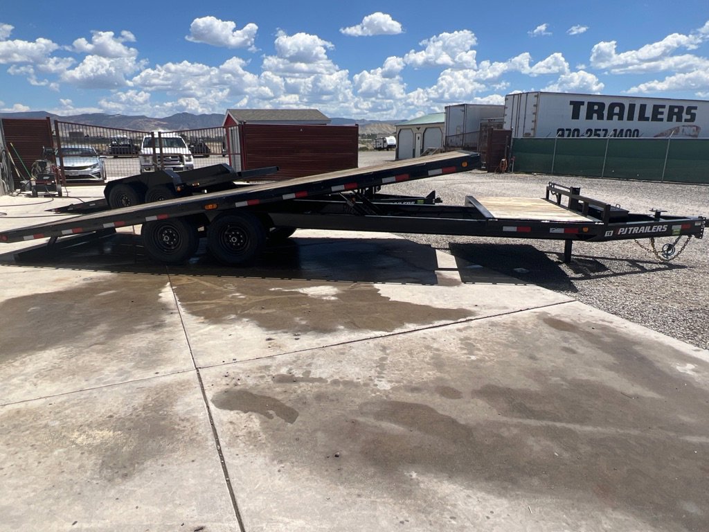 Black PJ tilt trailer with deck raised, parked on concrete trailer sales lot