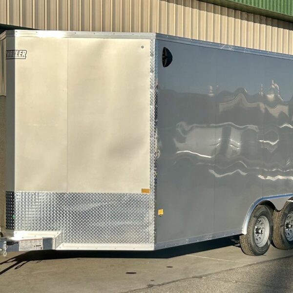 Silver enclosed Hauler trailer with dual axles and diamond plate front parked on concrete outside metal building under clear sky.