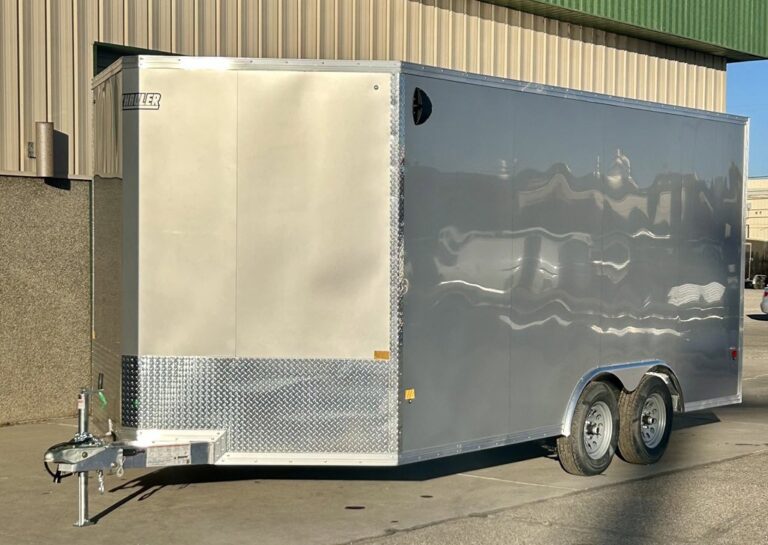 Silver enclosed Hauler trailer with dual axles and diamond plate front parked on concrete outside metal building under clear sky.