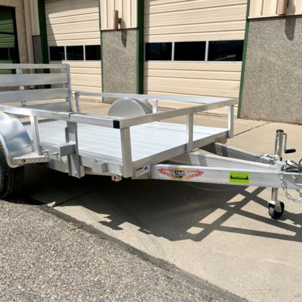 Aluminum utility trailer with open sides, black wheel, and rear ramp gate, parked on concrete near a building.