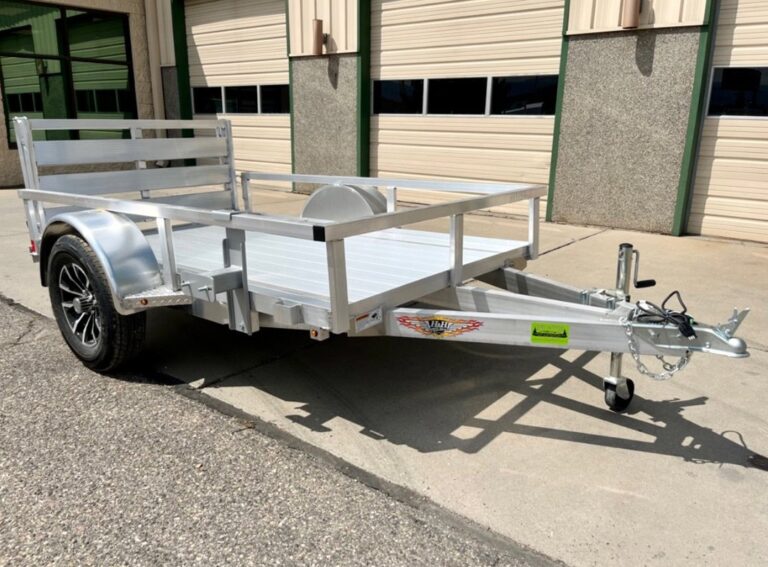 Aluminum utility trailer with open sides, black wheel, and rear ramp gate, parked on concrete near a building.