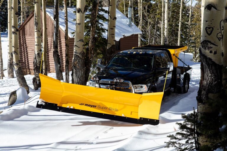 Black pickup truck with a large yellow Meyer Super Blade snow plow attached to the front and a yellow salt spreader on the back, parked in a snowy forest clearing