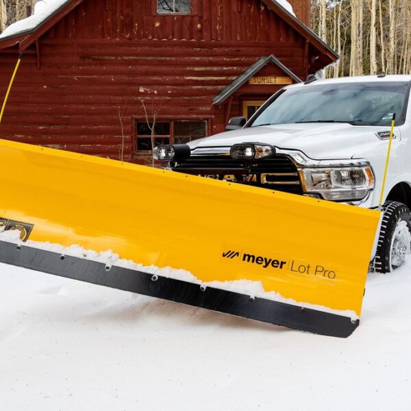 White truck with yellow Meyer Lot Pro snow plow clearing snow in front of red log cabin.