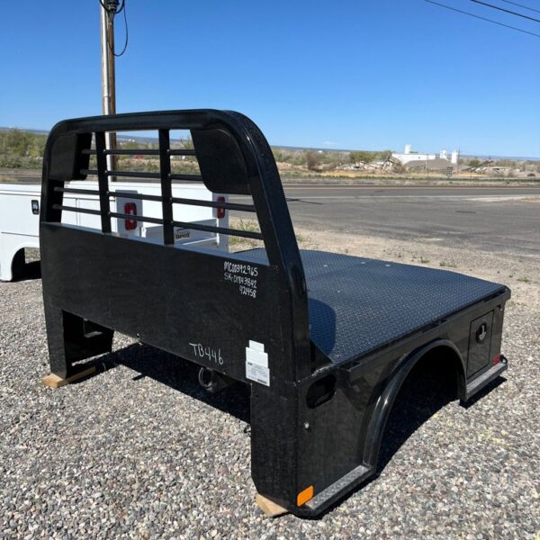 Black steel flatbed truck bed with diamond plate deck and headache rack parked on gravel lot