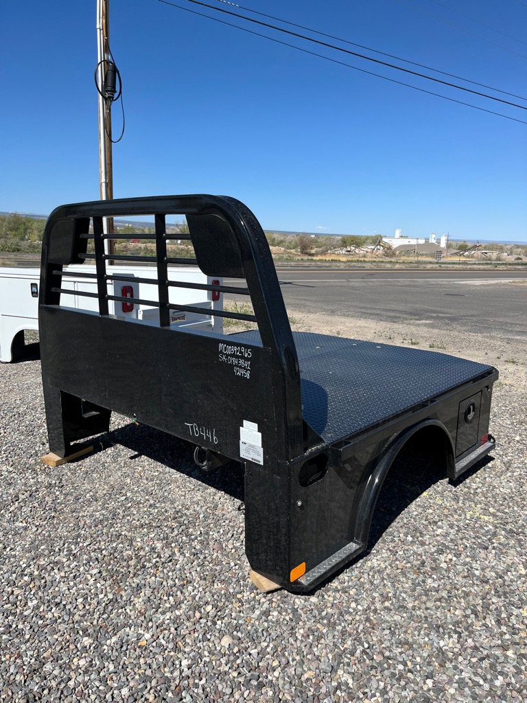 Black steel flatbed truck bed with diamond plate deck and headache rack parked on gravel lot