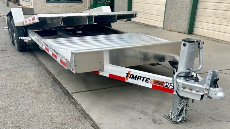 Aluminum Timpte car hauler trailer with tilt bed, red and white reflective tape, parked on concrete near garage doors.