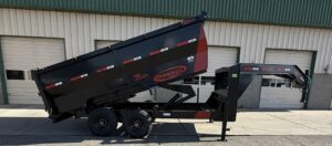 Dump trailer with the cargo area up in front of a large commercial garage.