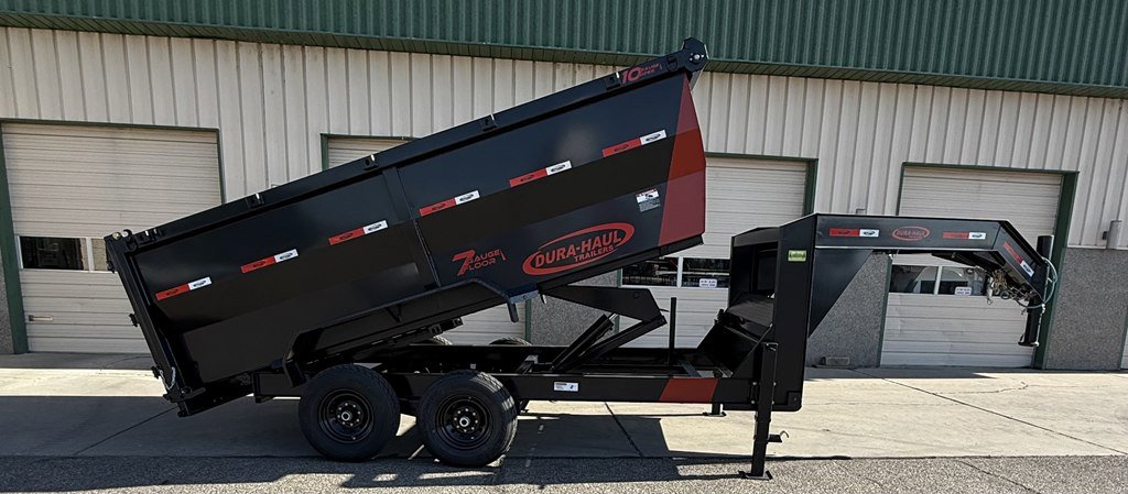 Dump trailer with the cargo area up in front of a large commercial garage.